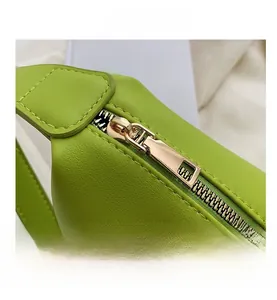 Detail of smooth gold metal zipper on textured green leather tote bag shoulder strap