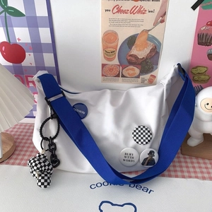 Detail of white canvas messenger bag with blue fashion badges and checkered bear charm