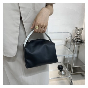Detail of minimalist black box handbag featuring white contrast handle and top zipper