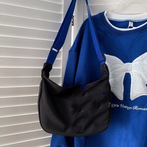 Close-up of black crescent messenger bag featuring a vibrant blue wide fabric shoulder strap