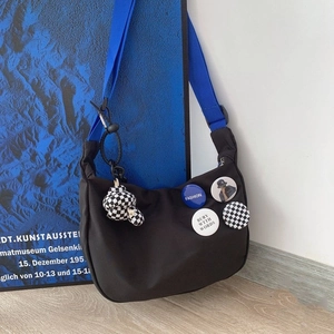 Detail of black nylon messenger bag with blue strap, pins, and checkerboard bear charm