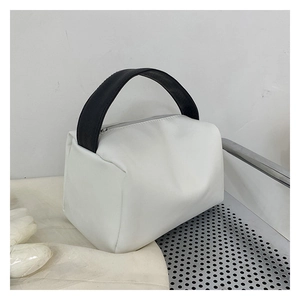 Detail of white leather-textured handbag featuring black wide handle and zipper closure