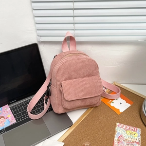Pink corduroy mini backpack detail showing textured fabric and front pocket on desk
