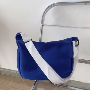 Detail view of Klein blue nylon crossbody bag with wide white adjustable strap on a chair