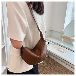Brown semi-circle shoulder bag shown as an underarm bag on a model in a modern room