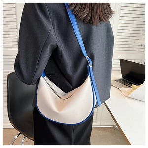Chic cream hobo bag with blue trim shown on shoulder in a stylish office setting