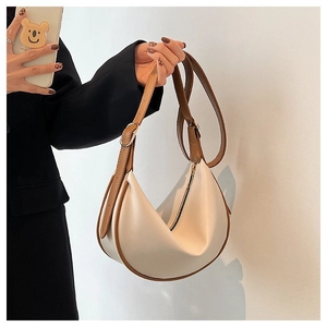 Minimalist cream crescent bag featuring brown adjustable strap and top zipper detail