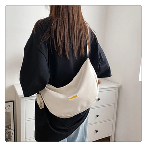 Detail of a beige crescent crossbody bag worn over a black t-shirt for daily casual style
