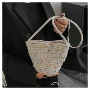 Detail of hand-woven straw bucket bag featuring colorful embroidery and pearl closure
