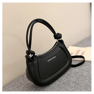 Detalle de bolso media luna en cuero sintético negro con asa anudada y texto de moda