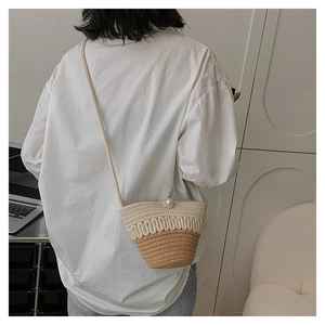 Detail of straw bucket bag featuring large pearl closure and two-tone woven texture