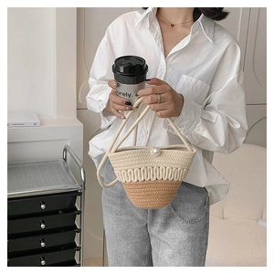 Detail of a straw bucket bag featuring two-tone weaving and a large decorative pearl