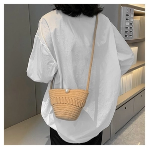 Detailed view of woven straw bucket bag with elegant pearl clasp and textured pattern