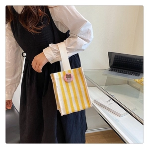 Vertical yellow and white striped canvas tote bag with a cute pink badge on office desk