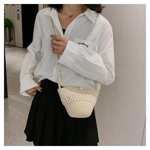 Detail of woven straw bucket bag featuring a central pearl buckle and textured finish