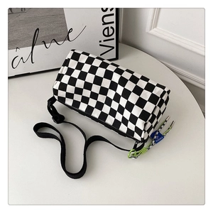 Détail macro du sac cylindrique en toile à damier avec sangle tissée et breloque déco