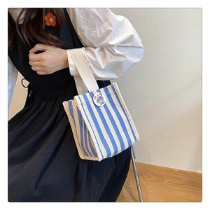 Detailed view of striped canvas tote bag with round badge carried by model in white shirt