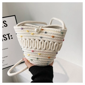 Detail of woven white cotton bucket bag featuring colorful pom-poms and a pearl clasp