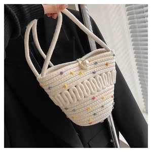 Detail of white woven bucket bag with colorful pom-poms and large pearl closure