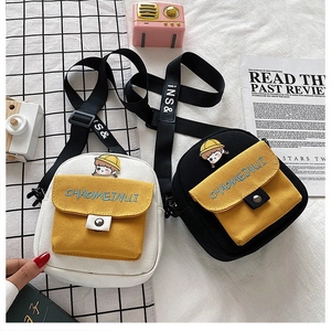 Primer plano de bolso bandolera de lona con parche de dibujos y detalle de bolsillo amarillo