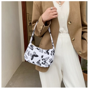 Detail of white baguette bag with black butterfly print worn by a model in soft lighting