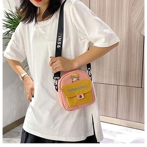 Detalle de un bolso bandolera de lona rosa y amarillo llevado por una modelo en un interior