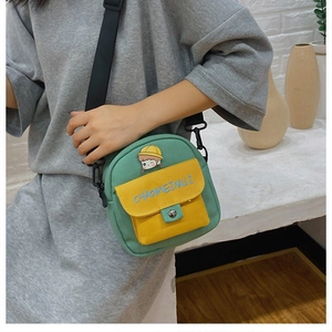 Primer plano de bolso bandolera de lona verde con solapa amarilla y parche de niña linda