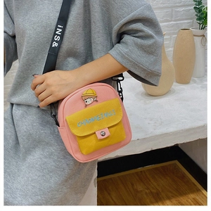 Detalle del bolso bandolera de lona rosa y amarillo con insignia de dibujos y correa ajustable