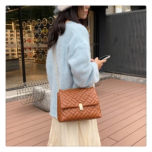 Close-up of brown quilted leather shoulder bag with gold chain strap on a fashion model