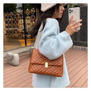 Detail of caramel quilted chain bag with gold buckle on blue fuzzy sweater