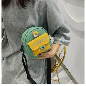 Detalle de bolso bandolera de lona verde y amarillo con dibujo de niña y correa