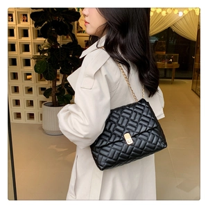 Chic black quilted shoulder bag with gold chain strap worn by a model in casual attire