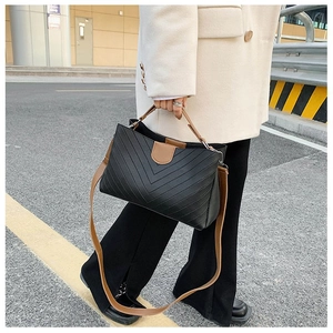 Detail of black V-quilted faux leather bag with brown strap and silver hardware