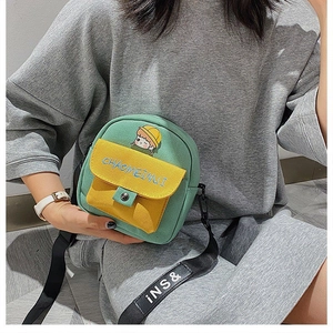 Detalle del pequeño bolso bandolera de lona verde y amarillo con parche de dibujos