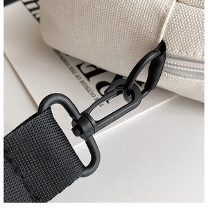 Detalle de mosquetón metálico negro mate y tela de lona beige en bolso pequeño de bandolera