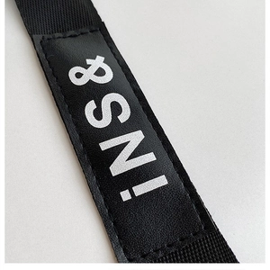 Detalle de la correa de nailon negro con parche de cuero sintético y letras INS blancas