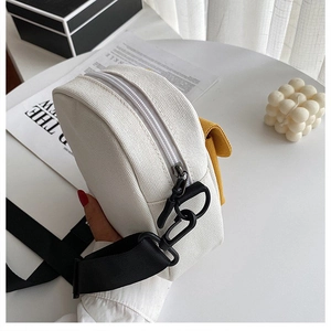 Detalle de bandolera de lona blanca con bolsillo amarillo y correa negra tejida