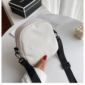 Detalle del mini bolso bandolera de lona blanca con correa negra sobre una mesa minimalista