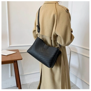 Detail of a black crossbody bag with V-shaped quilting and adjustable strap on a model