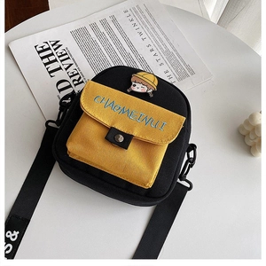 Detalle del bolsillo de lona amarilla con pin de dibujos y bordado en bolso bandolera negro