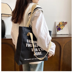 Detail of black canvas tote bag showing large white font and beige carrying handles