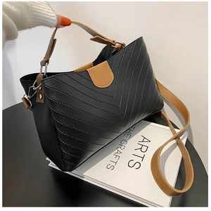 Minimalist V-quilted black shoulder bag with brown strap on a white book surface