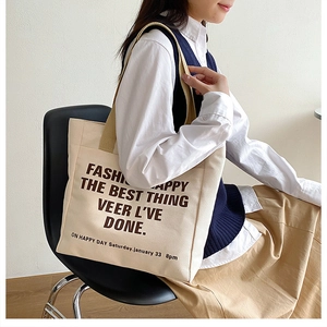 Detail of minimalist cream canvas tote bag with brown text and wide shoulder strap