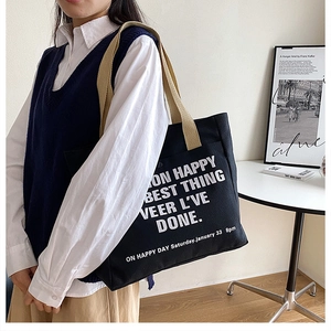 Detail of black canvas tote bag with white lettering and brown shoulder straps