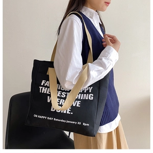 Detail of black canvas tote bag with white lettering and sturdy beige straps