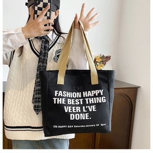 Detail of black canvas tote bag showing large white lettering and convenient front pocket