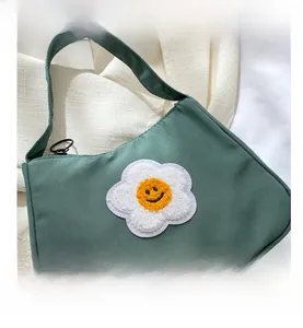 Detail view of green baguette bag with sunflower plush embroidery and black zipper