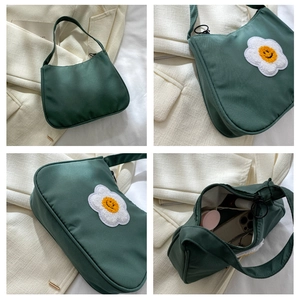 Detail view of a green nylon baguette bag with daisy embroidery holding daily essentials