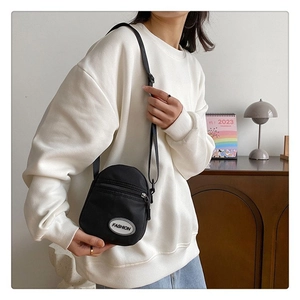 Detalle de bolso bandolera de lona negra con etiqueta Fashion sobre sudadera blanca