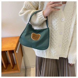 Detail of dark green nylon handbag featuring a cute brown plush bear patch and zip closure